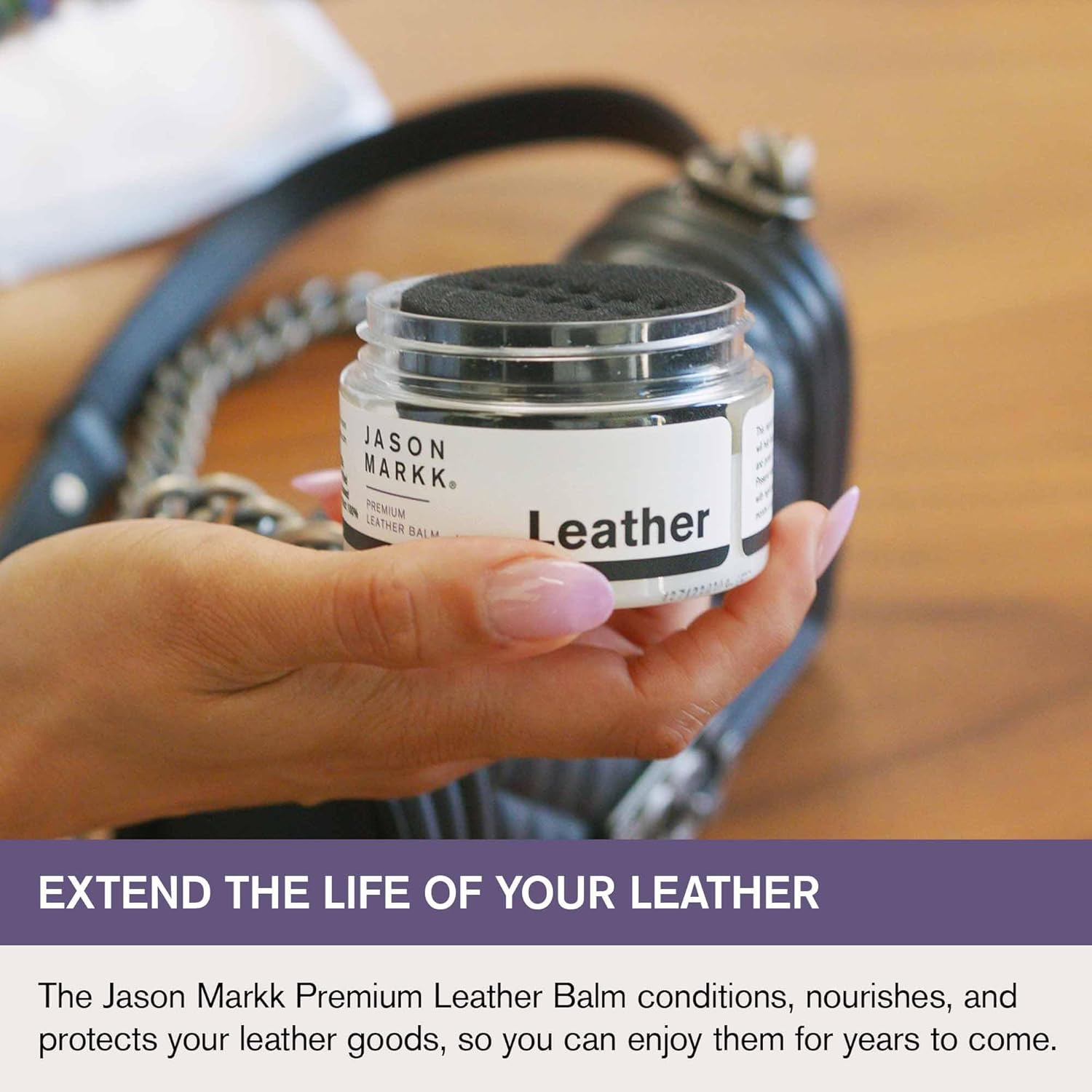 Hand holding a jar of Jason Markk Leather Balm with a leather product in the background.
